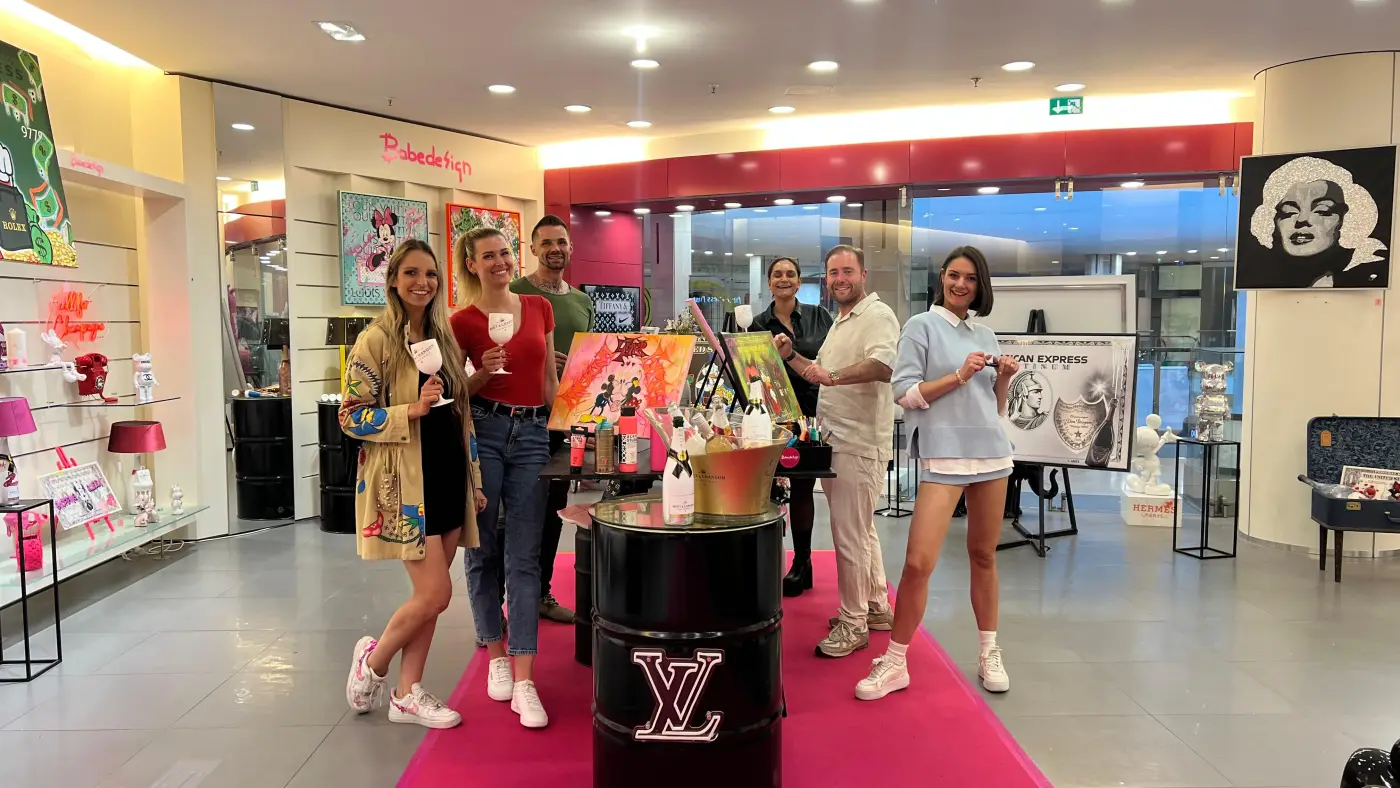 Malevent mit Babedesign: Gäste mit ihren selbst gemalten Bildern lachen in die Kamera, im Hintergrund die Babedesign-Galerie mit Pop-Art-Werken