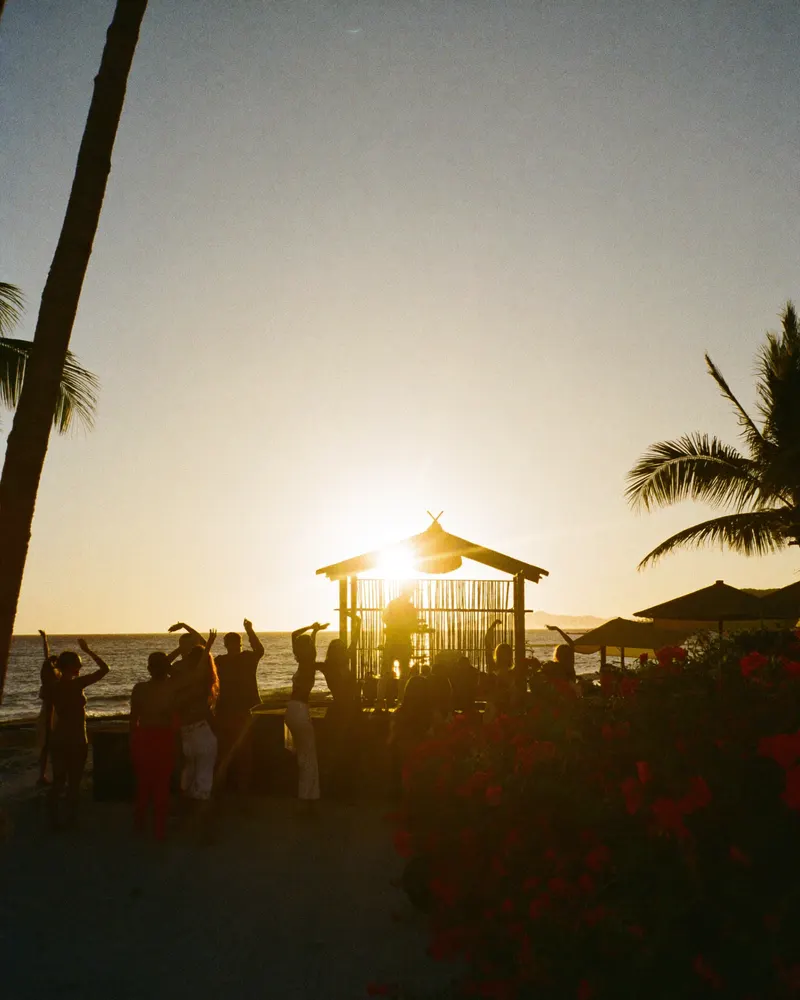 AI-generated image: silhouettes of a crowd at a beach club event against the evening light